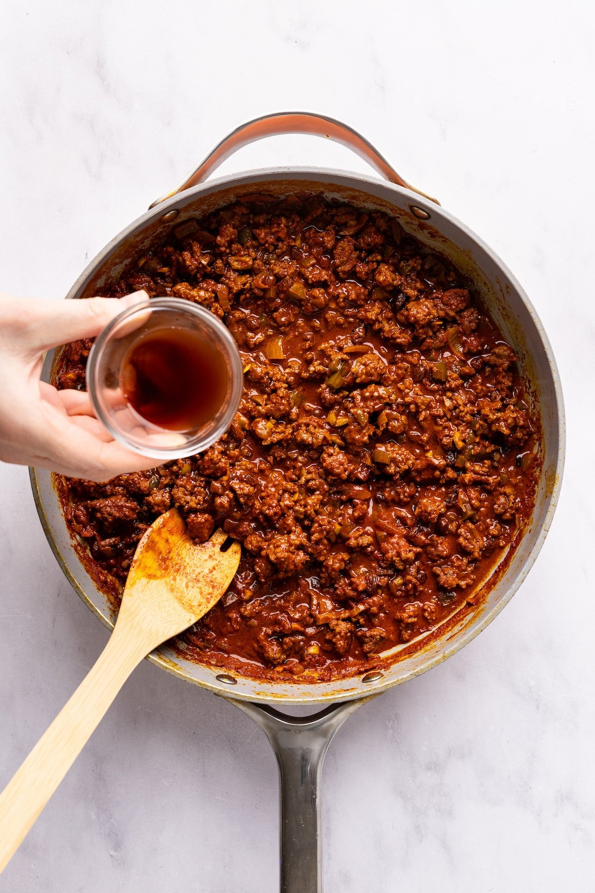 pouring vinegar into large skillet with cooked picadillo
