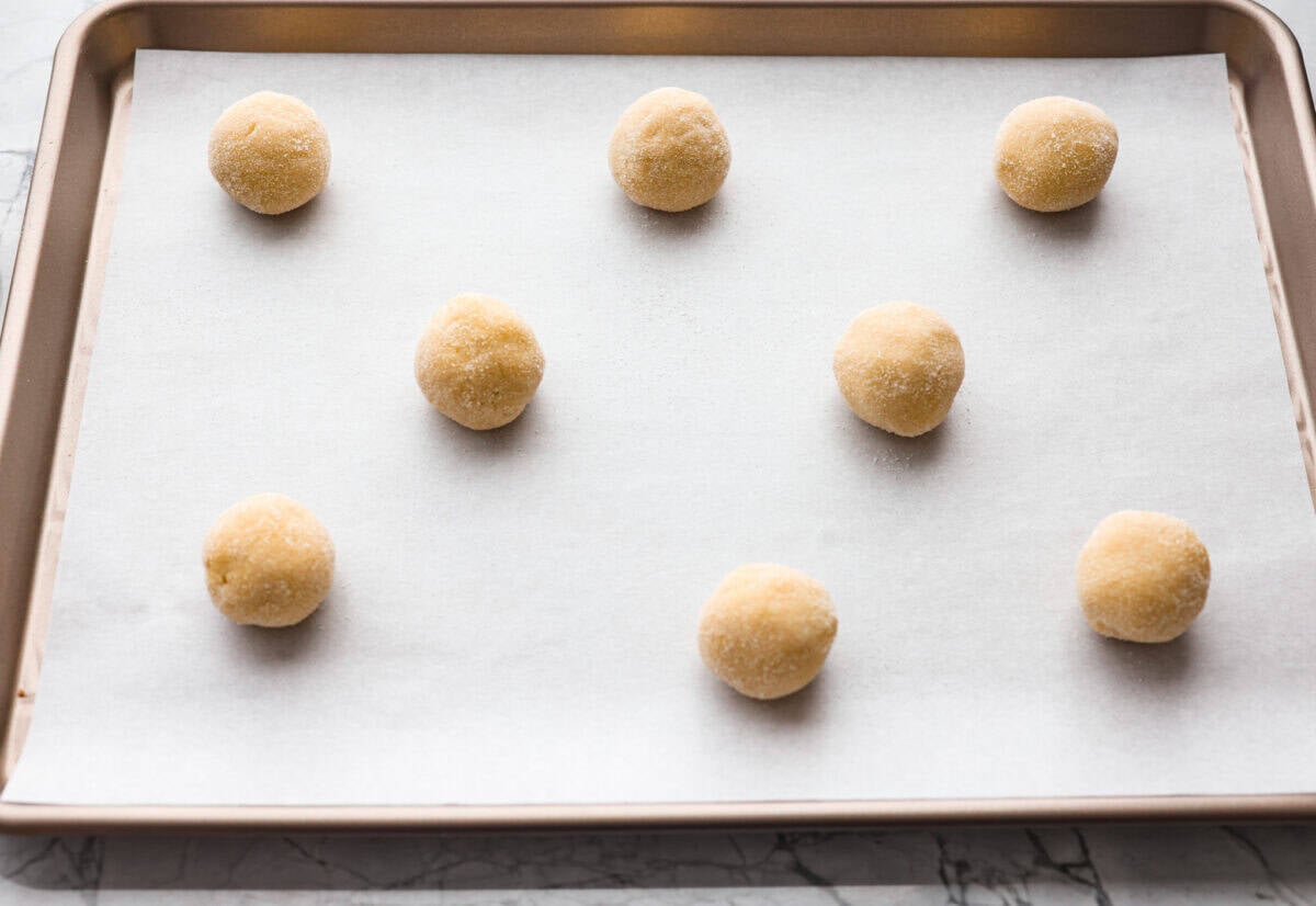 Balls of dough rolled out and in sugar and placed on parchment paper on a cookie sheet.