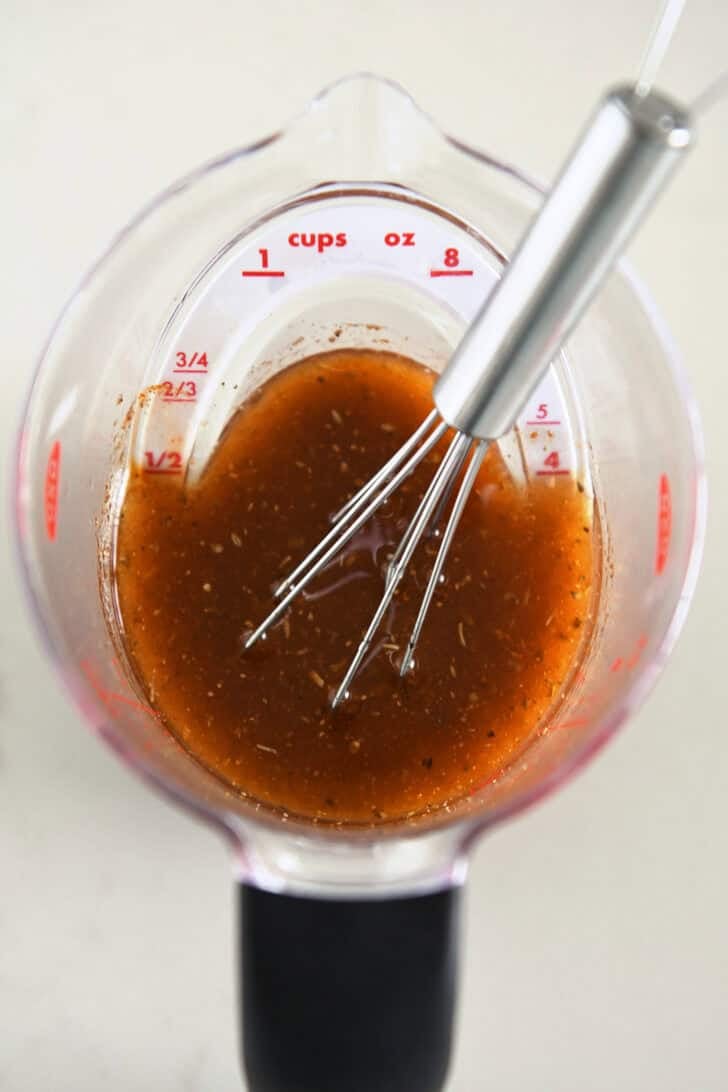 Liquid measuring cup with chicken marinade and small whisk.