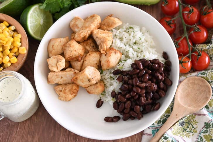 White bowl with cilantro lime rice, cooked chicken and black beans.
