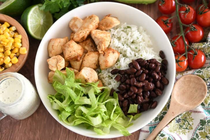 White bowl with cooked chicken, cilantro lime rice, black beans and lettuce.