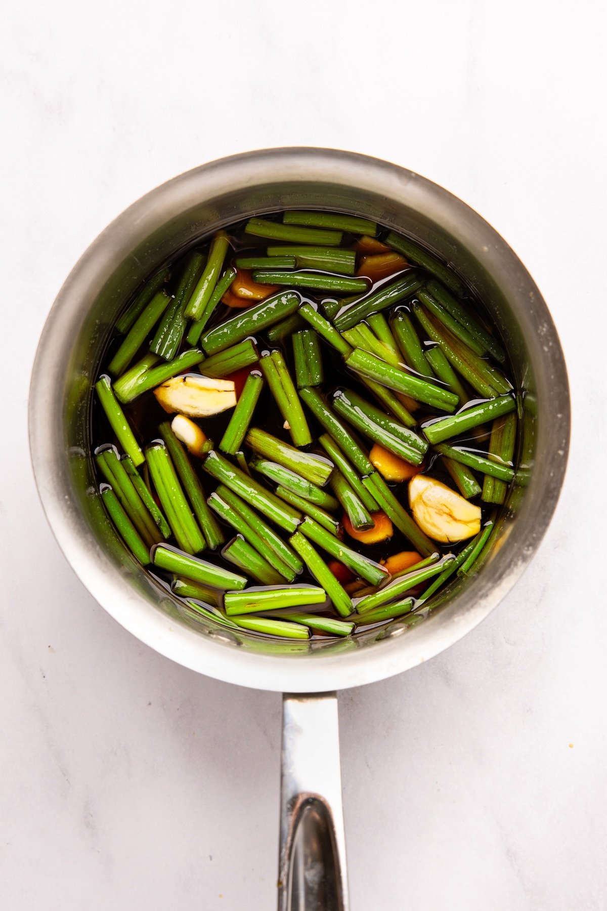 small saucepan with soy sauce, mirin, sake, brown sugar, ginger, garlic, and dark green scallions