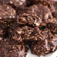 Stack of chocolate no-bake cookies on white plate with one cookie broken in half.