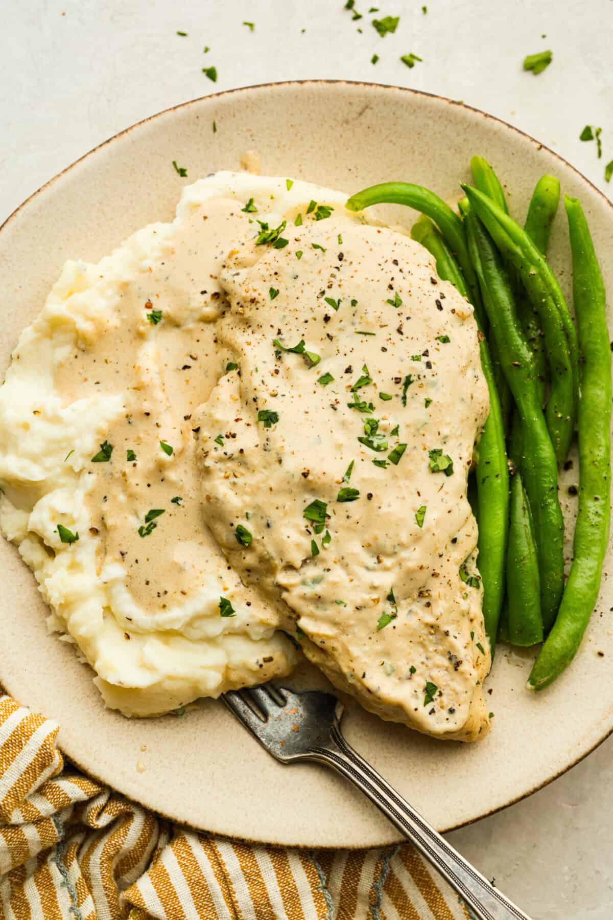 Plated cream cheese chicken with mashed potatoes and green beans. 