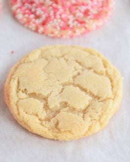 Baked sugar cookie on sheet pan next to cookies with sprinkles.