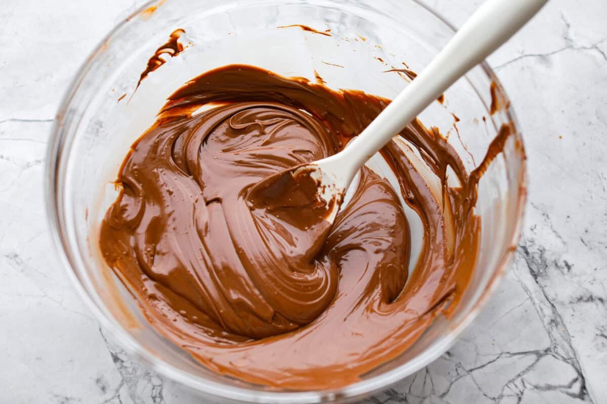 This 3 Ingredient Cool Whip Candy tastes just like a Three Musketeers! Fluffy on the inside, smooth chocolate on the outside, and so easy to make. It is the kind of treat you stash in the freezer and keep sneaking for yourself! Melted chocolate stirred and smoothed out in a mixing bowl.