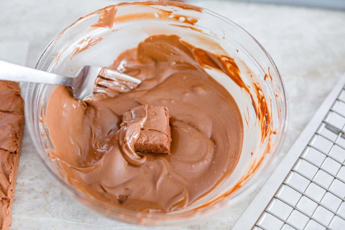This 3 Ingredient Cool Whip Candy tastes just like a Three Musketeers! Fluffy on the inside, smooth chocolate on the outside, and so easy to make. It is the kind of treat you stash in the freezer and keep sneaking for yourself! Someone dipping the pieces of fluffy filling into the melted chocolate to coat it.
