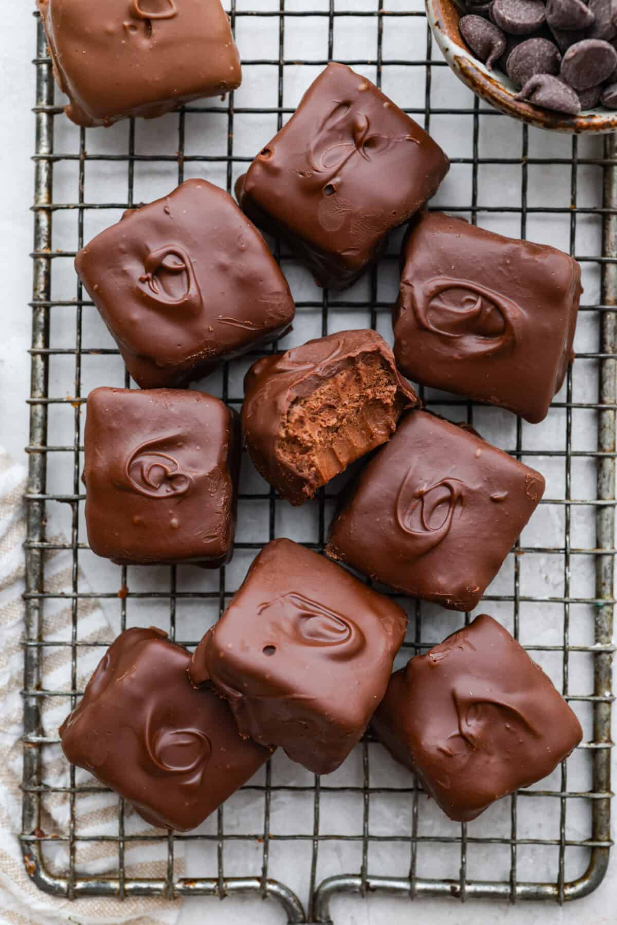 This 3 Ingredient Cool Whip Candy tastes just like a Three Musketeers! Fluffy on the inside, smooth chocolate on the outside, and so easy to make. It is the kind of treat you stash in the freezer and keep sneaking for yourself! Cool whip candy pieces on a cooling rack with one on its side with a bite taken out.