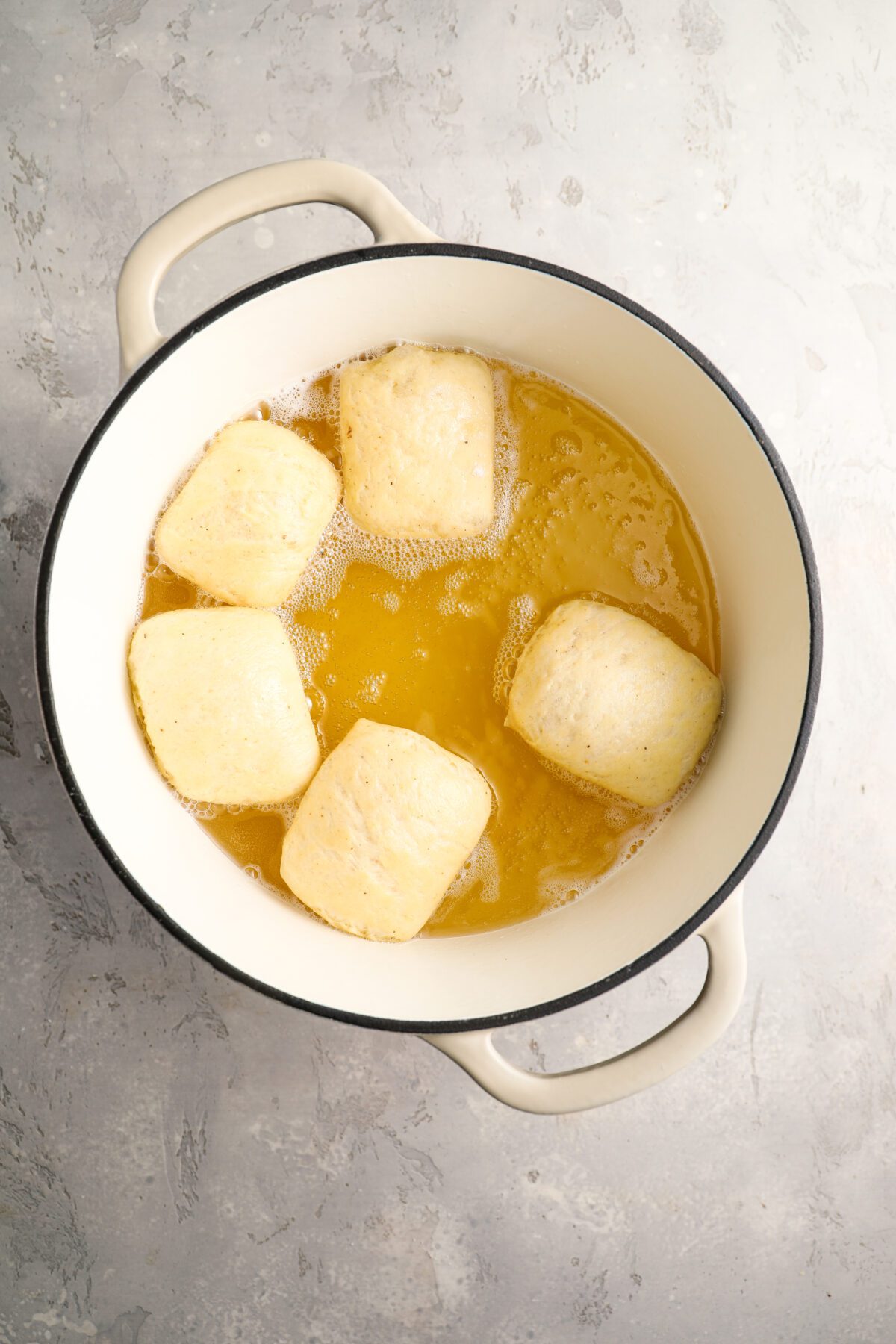 5 uncooked beignets in large dutch oven with hot oil