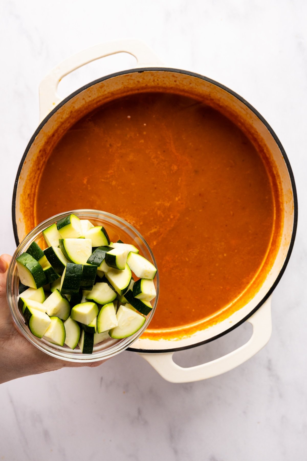 adding diced zucchini to dutch oven with albondigas soup
