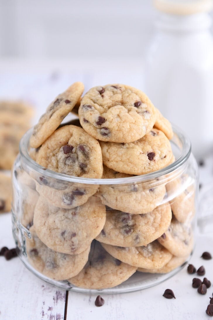 Glass jar filled with mini chocolate chip cookies with mini chocolate chips around bottom.