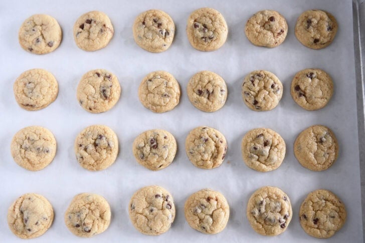 Top down view of 24 mini chocolate chip cookies on parchment lined baking sheet.