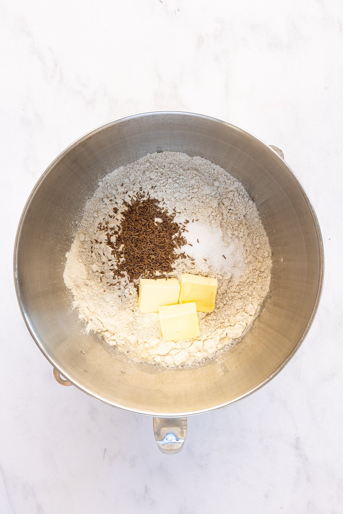 mixing bowl with salt, bread flour, rye flour, caraway seeds, and butter added to the water/honey mixture