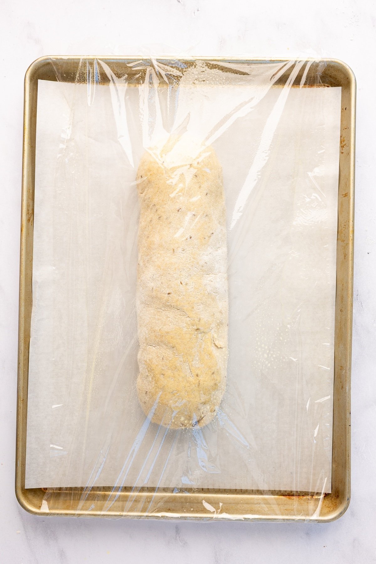rye loaf on parchment lined baking sheet covered with plastic wrap 