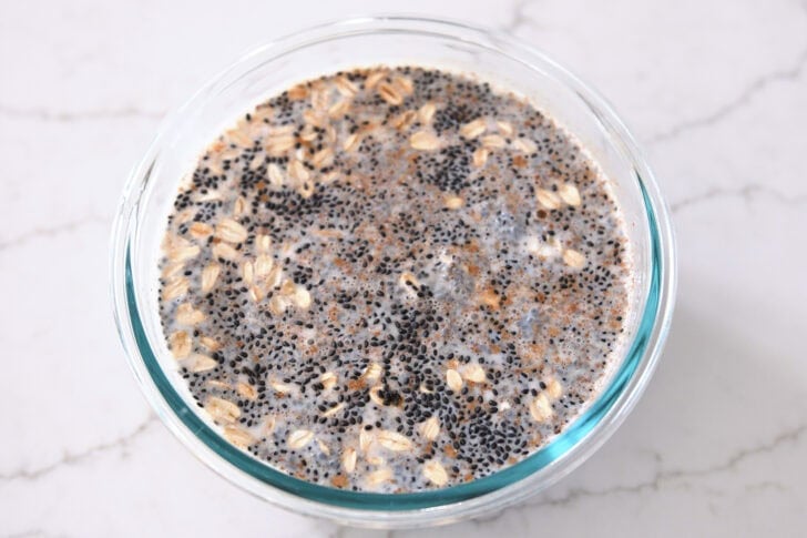 Glass bowl with almond milk, chia seeds, basil seeds, oats, cinnamon, maple syrup and salt.