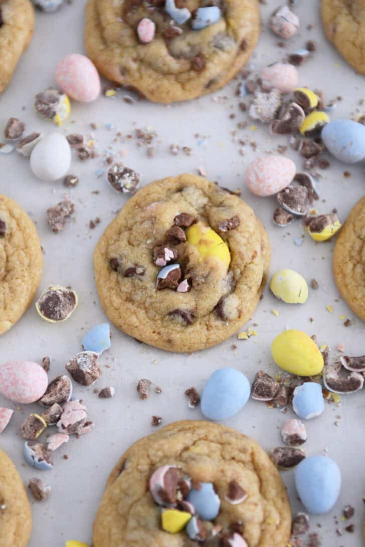 Baked cookies on parchment paper with crushed and whole cadbury eggs scattered around.
