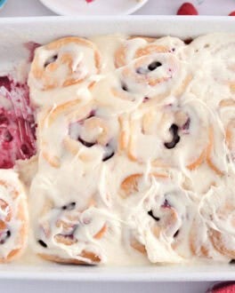 White 9X13-inch pan of baked raspberry sweet rolls spread with sweet cream cheese icing.