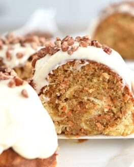 A slice of carrot and cream cheese swirled bundt cake being taken off a white plate with a white spatula.