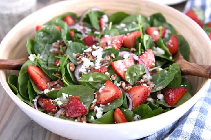 Wooden salad bowl with fresh spinach, sliced strawberries, sliced red onions, feta cheese, chopped pecans and poppy seed dressing.