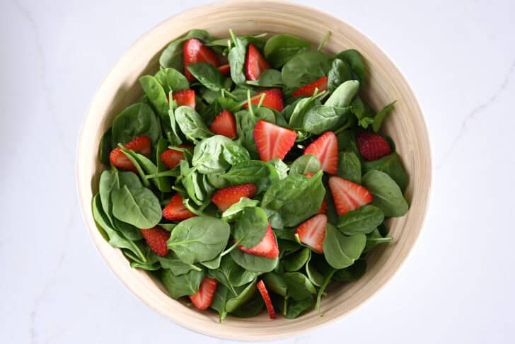 Wooden bowl with fresh spinach and sliced strawberries.