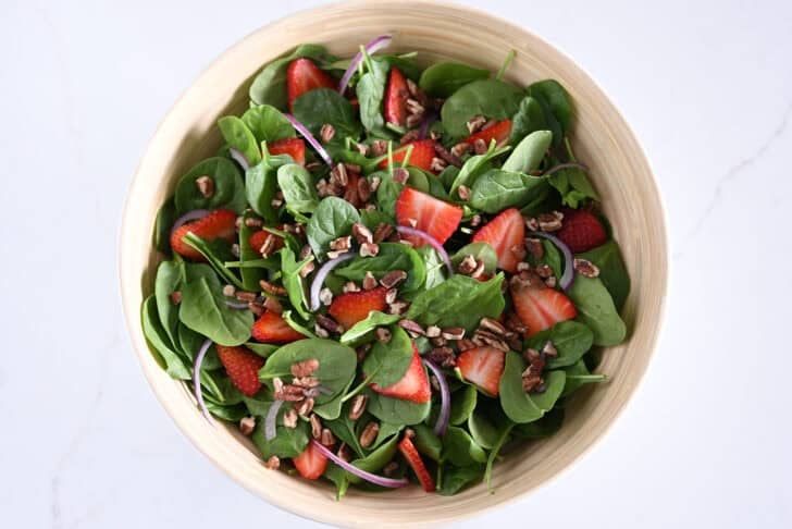 Wooden salad bowl with fresh spinach, sliced strawberries, sliced red onions, chopped pecans.