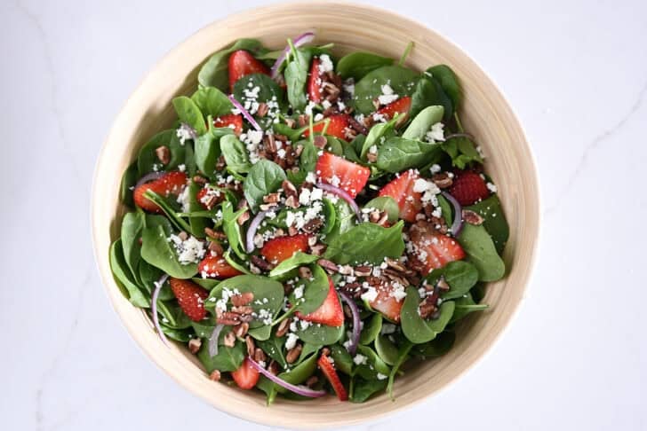 Wooden salad bowl with fresh spinach, sliced strawberries, sliced red onions, feta cheese, chopped pecans.