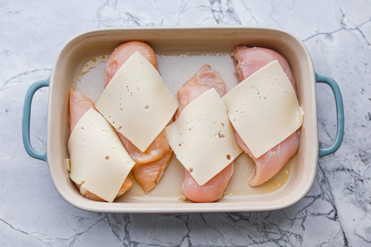 Chicken breasts in the bottom of a baking dish with a slice of Swiss cheese on top. 