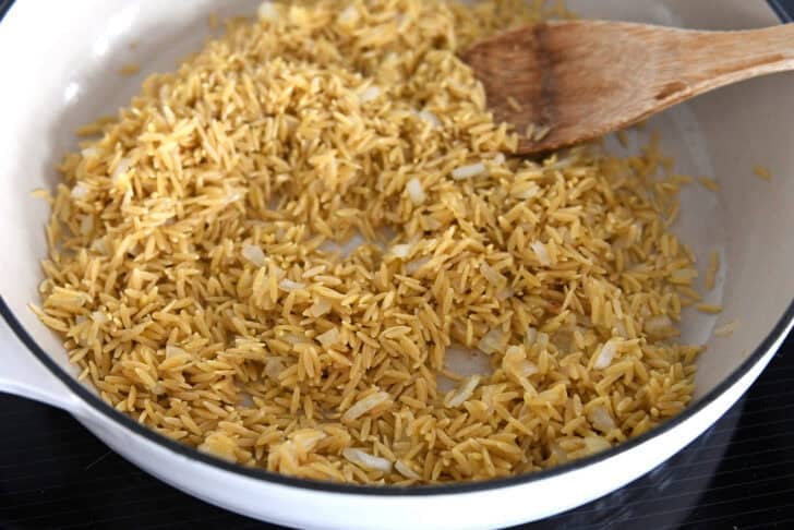 White pan with toasted orzo and onions.