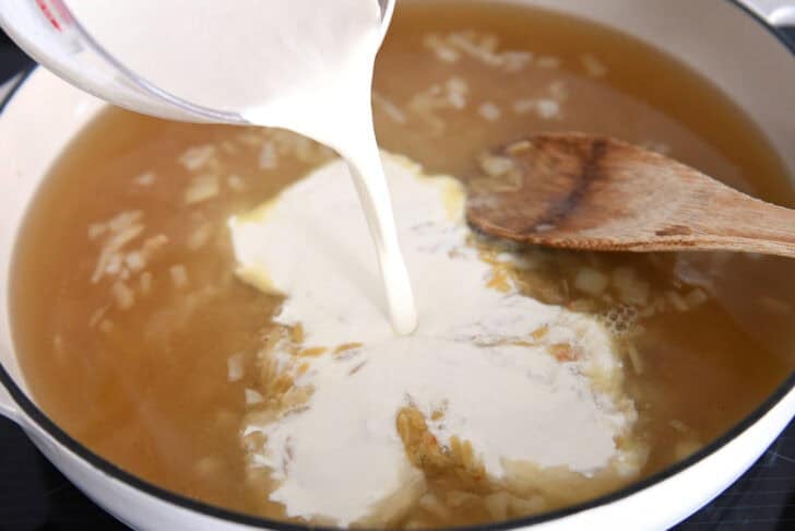 Pouring cream into white pan with broth and orzo.
