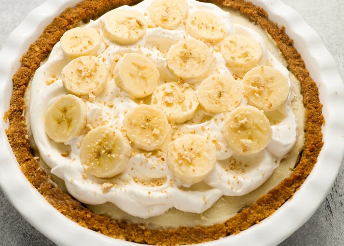 banana cream pie topped with whipped cream, banana slices, and nilla wafer crumbs
