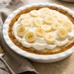 banana cream pie with a linen napkin and stack of plates