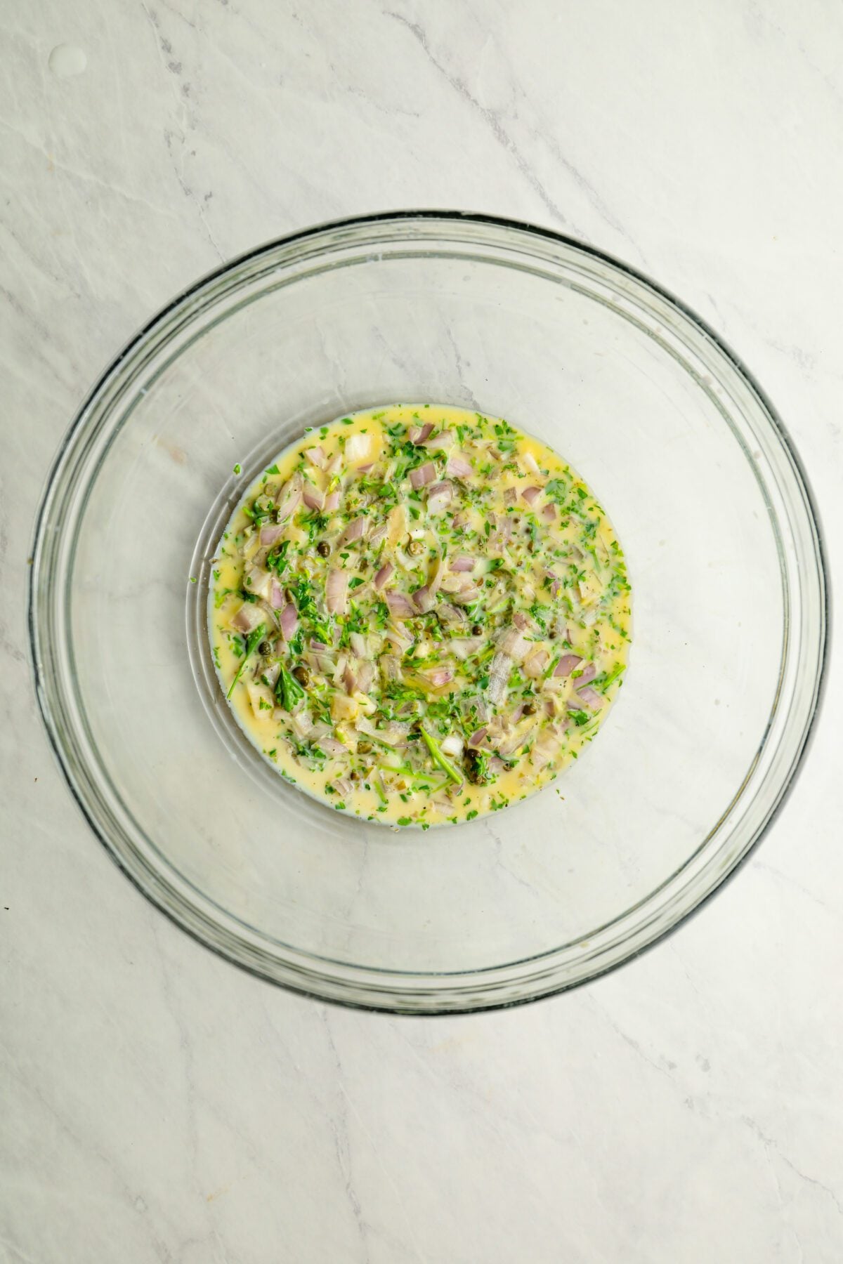 large glass bowl with egg, parsley, shallot, capers, garlic, milk, salt, and pepper