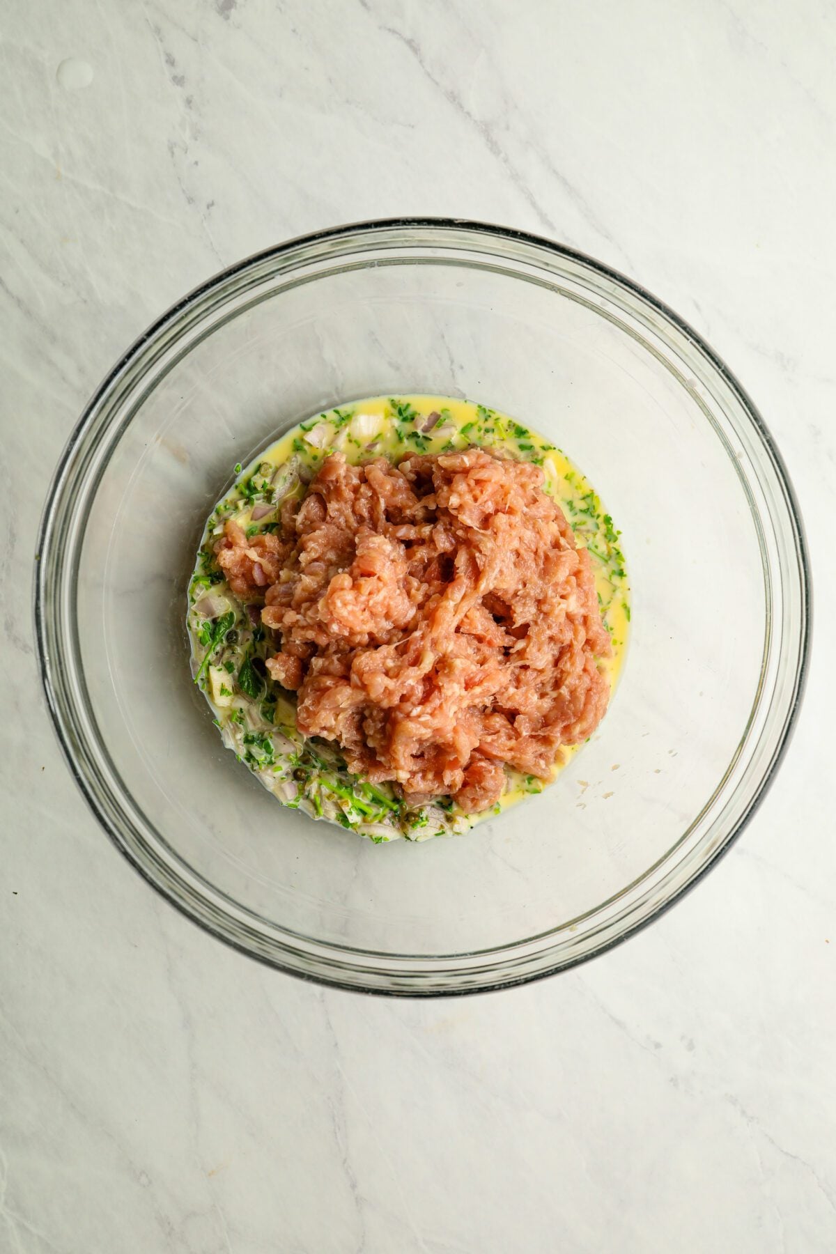 large bowl with ground chicken added to egg, parsley, shallot, capers, garlic, milk, salt, and pepper