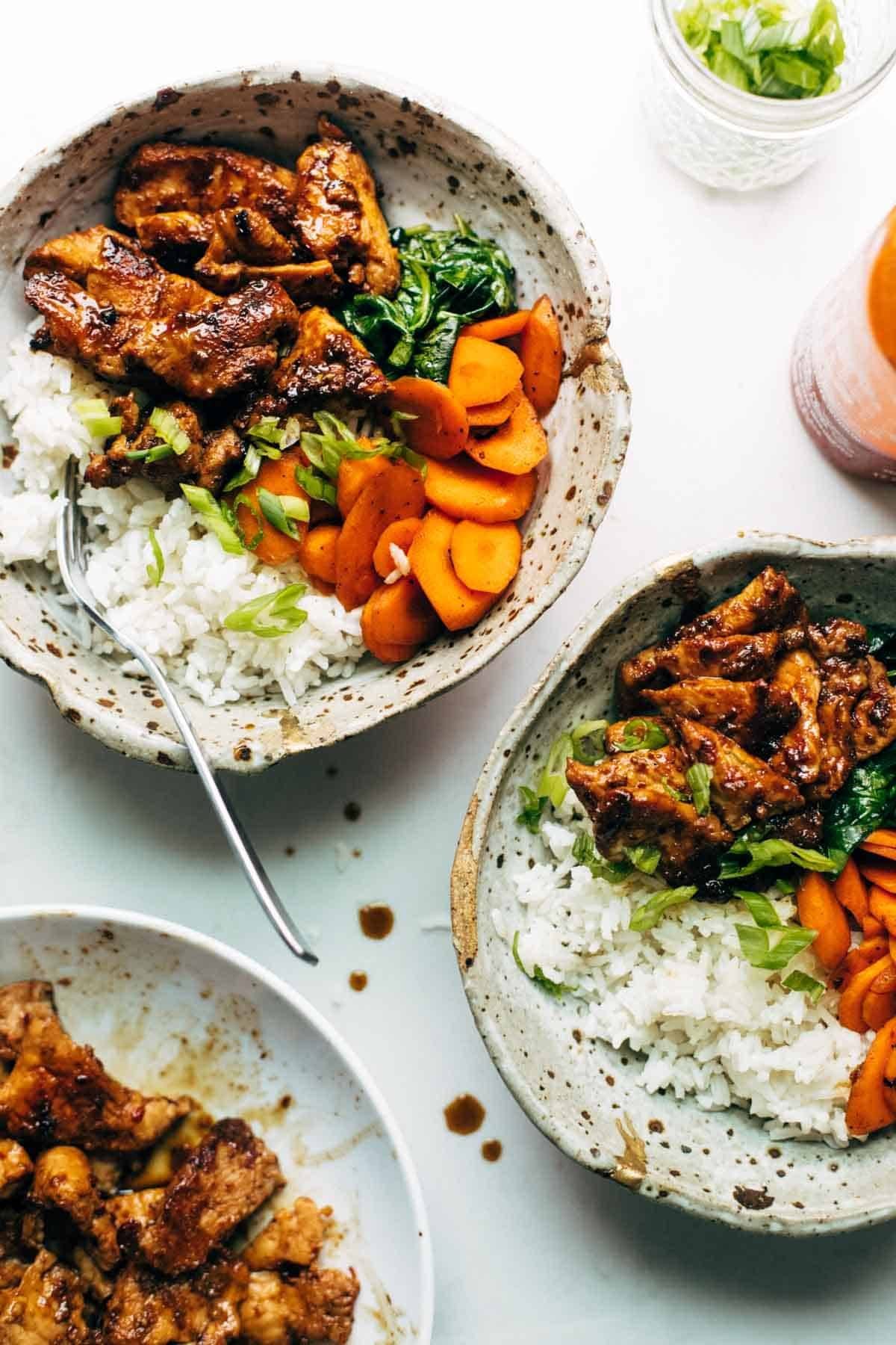 Spicy pork in a bowl with rice and veggies.