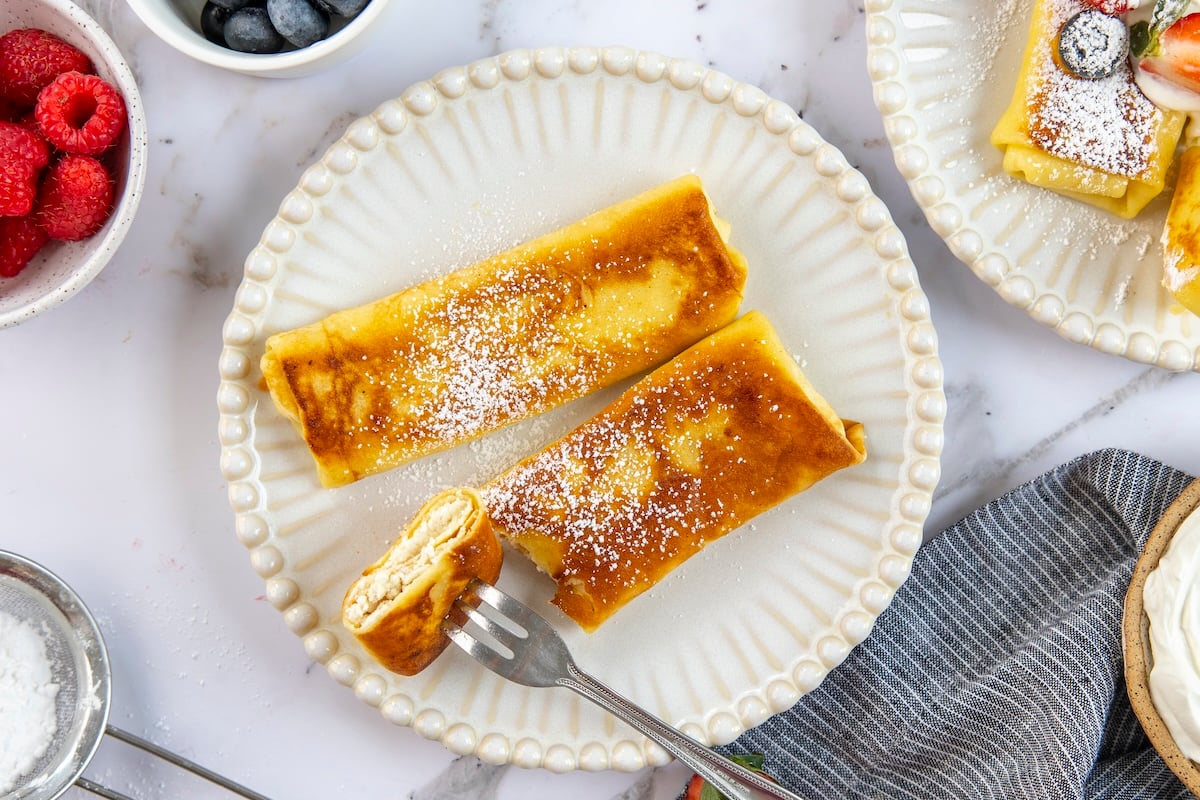 white plate with two confectioners' sugar-dusted blintzes
