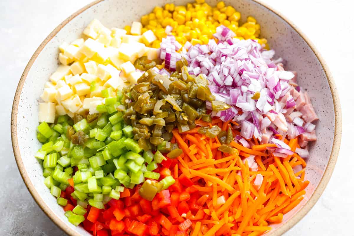 All of the cheese, veggies and other ingredients in a bowl that go in the salad. 
