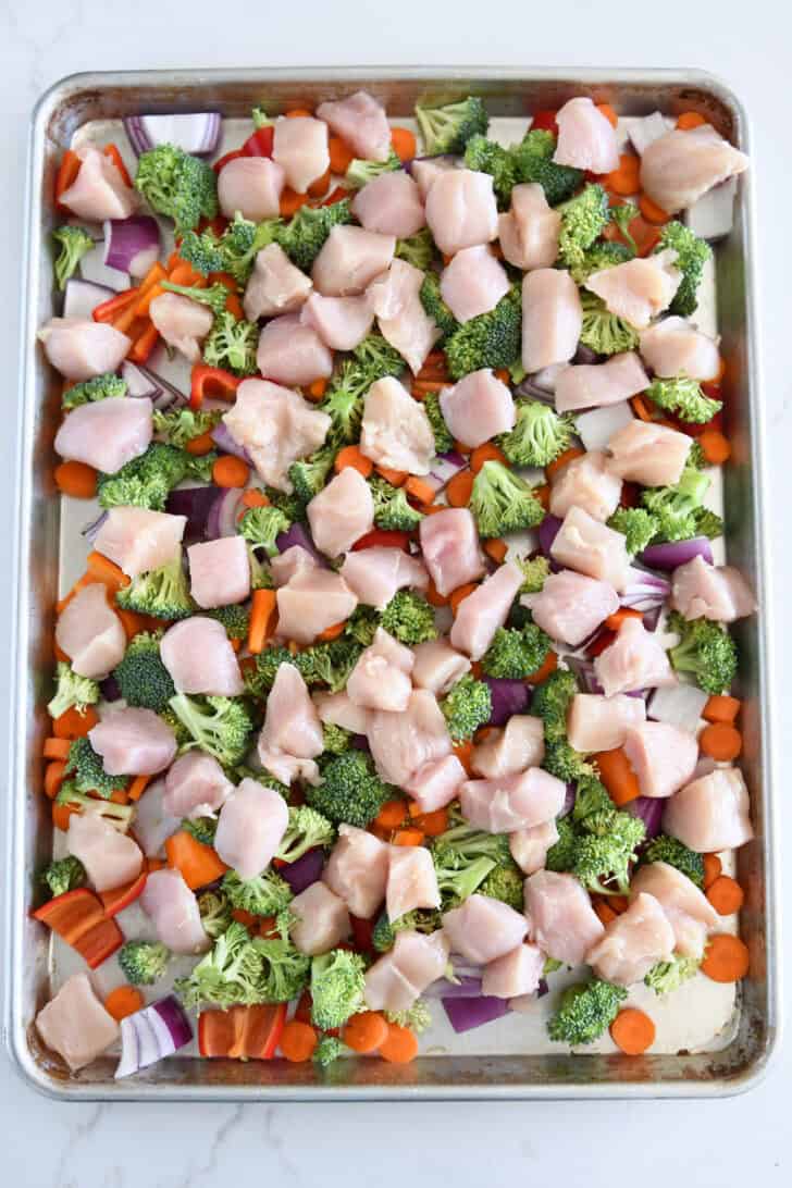 Sheet pan with red onions, carrots, bell peppers, chicken, and broccoli.