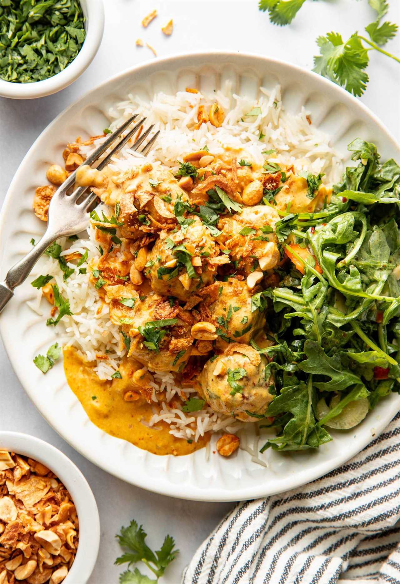 Yellow curry meatballs on a plate with rice and greens.