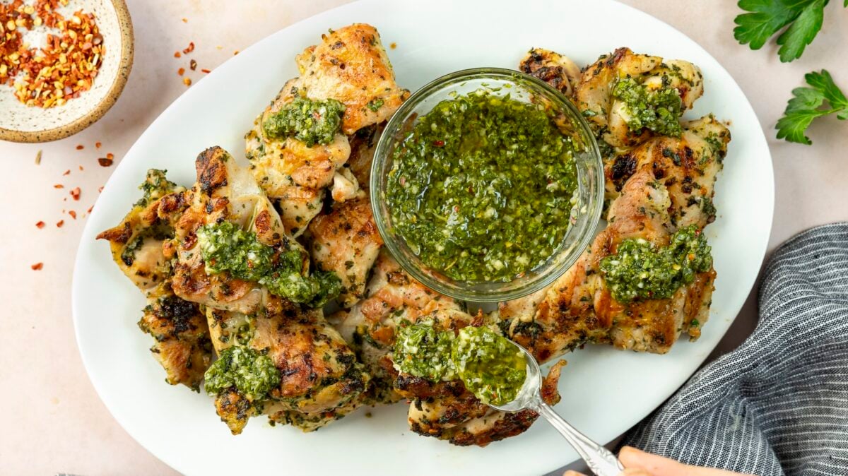large white platter with chimichurri chicken with bowl of chimichurri sauce positioned in between chicken pieces