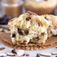 One almond coconut chocolate chip muffin broken in half on brown paper liner.