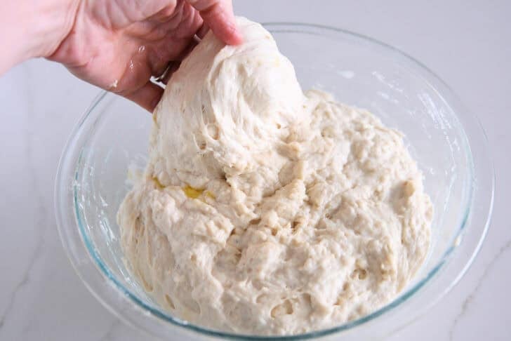 Stretching and folding focaccia dough in glass bowl.