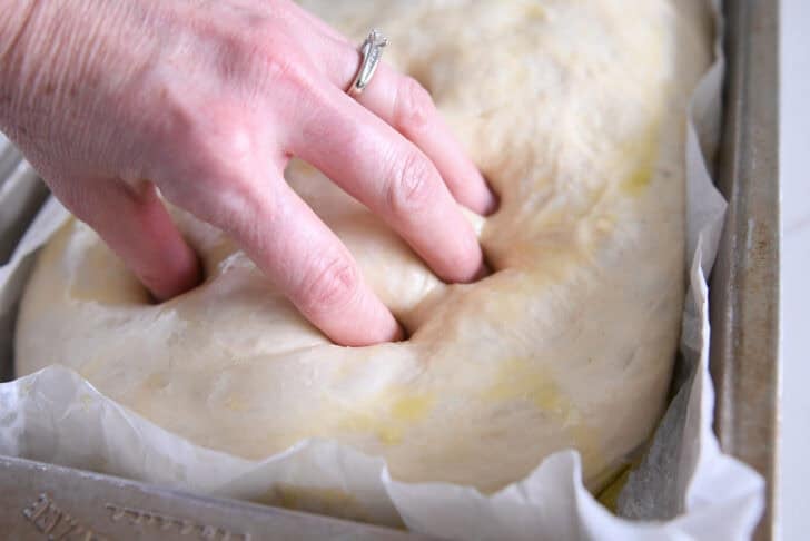 Using fingers to press dimples in olive oil-topped unbaked focaccia bread.