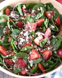 Wooden salad bowl with fresh spinach, sliced strawberries, sliced red onions, feta cheese, chopped pecans and poppy seed dressing.