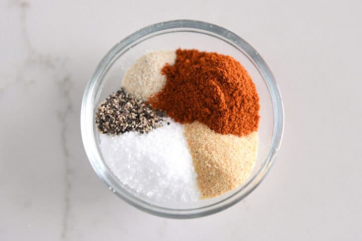 Black pepper, salt, onion powder, garlic powder, and paprika in glass bowl.