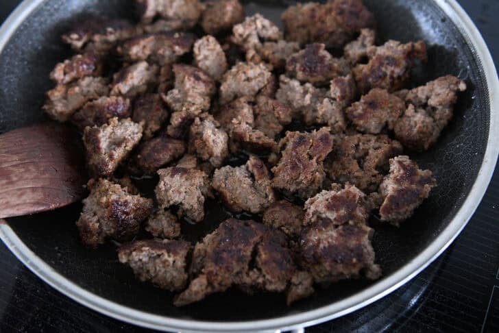 Chunks of crispy ground beef cooking in skillet.