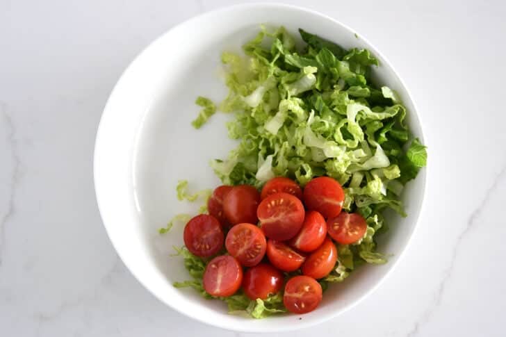 Top down view of lettuce and tomatoes in white bowl.