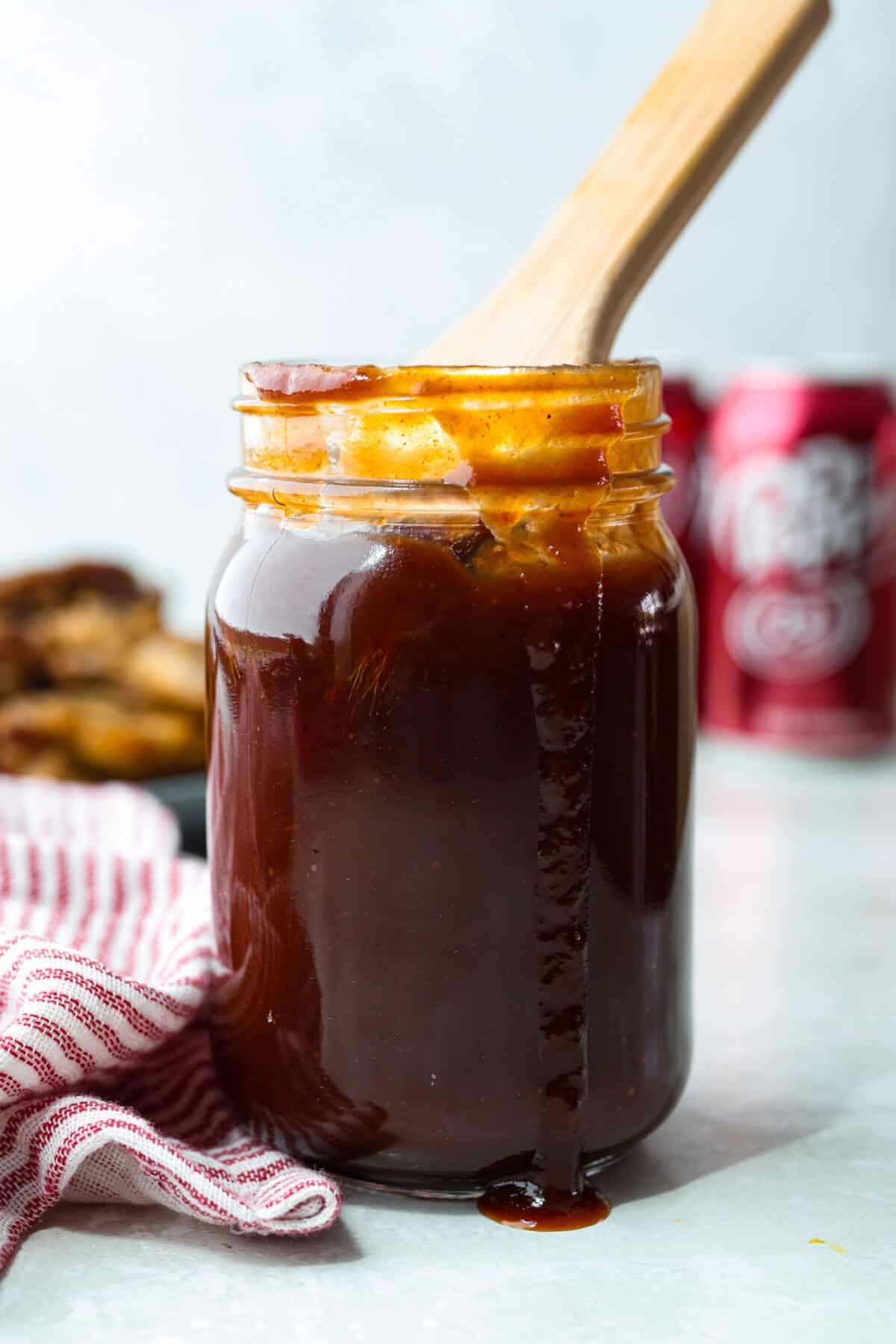 Bottle of Dr Pepper BBQ sauce with a wooden spoon sticking out of it, and cans of Dr Pepper in the background. 