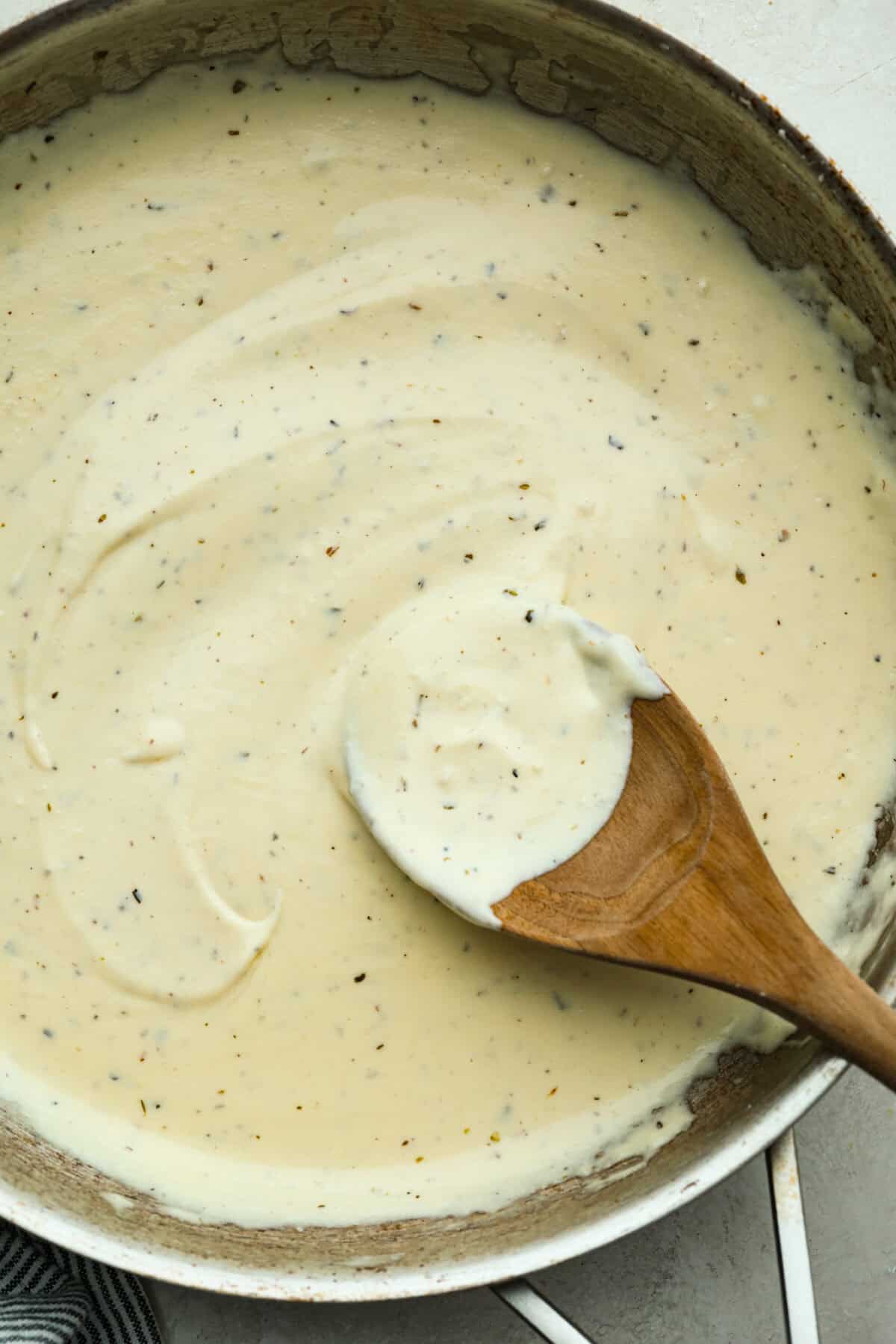 Pan of homemade Alfredo sauce with a wooden spoon.