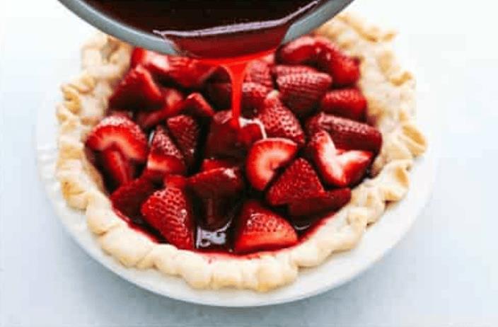 Pouring the strawberry glaze over the fresh strawberries in the pie crust. 