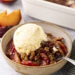 Plum crisp in a bowl with vanilla ice cream.